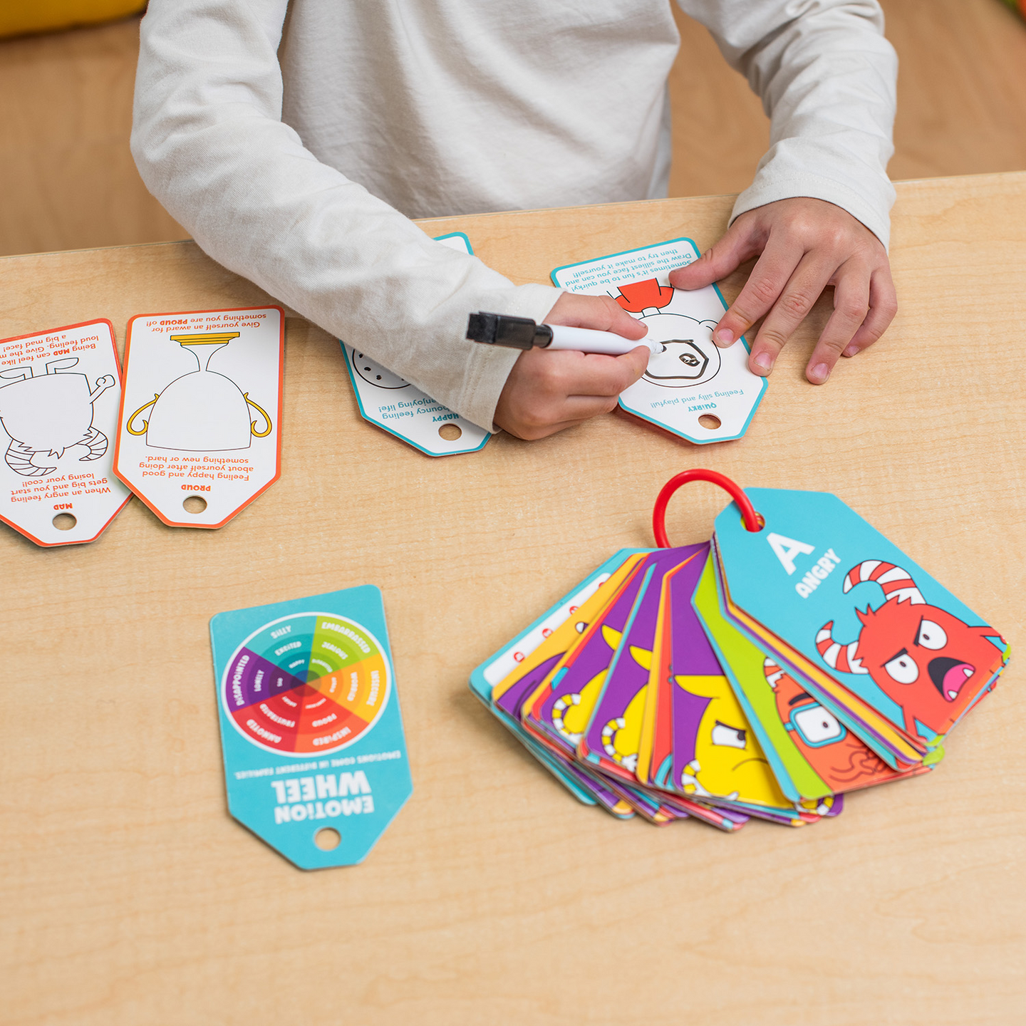 Hand writing on an Emotions ABC's dry-erase card with the deck fanned alongside