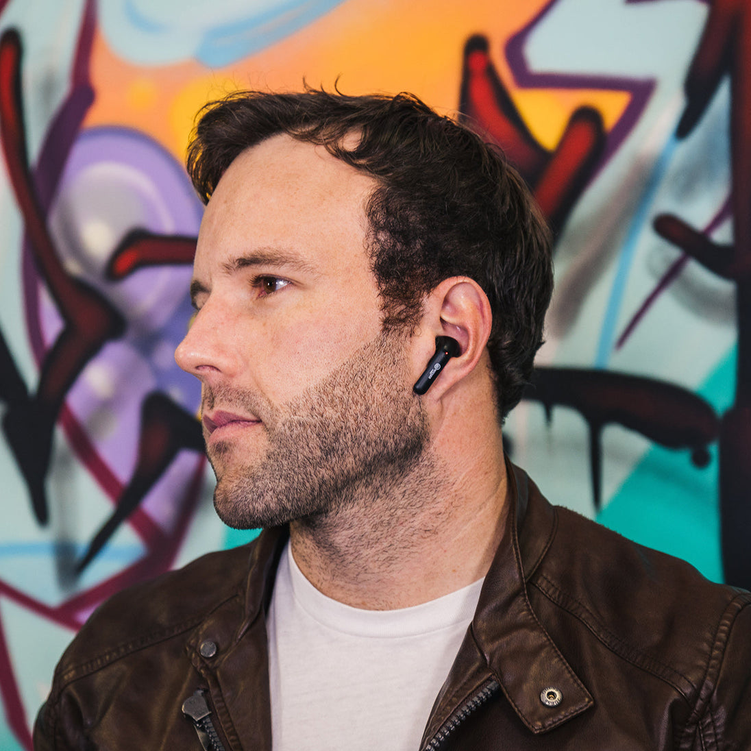 Man wearing Wicked Audio Mojo 500 earbuds in front of a graffiti wall