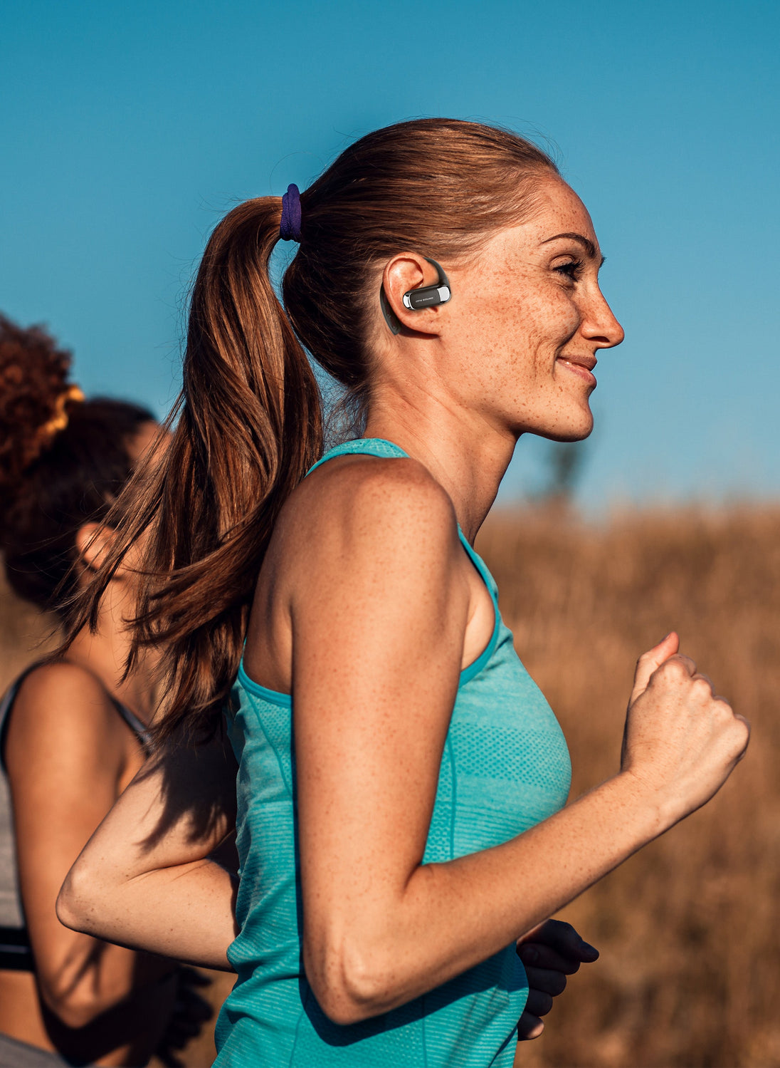 Woman running outdoors wearing OPN Sound Aria Pro headphones